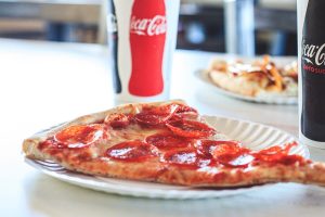 A slice of pizza on a plate next to a cup of coca cola.